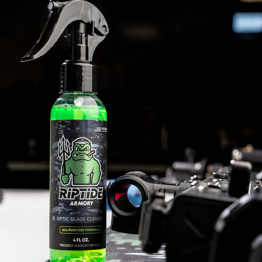 Bottle of Riptide Armory Optic Cleaner on a table equipment in the background