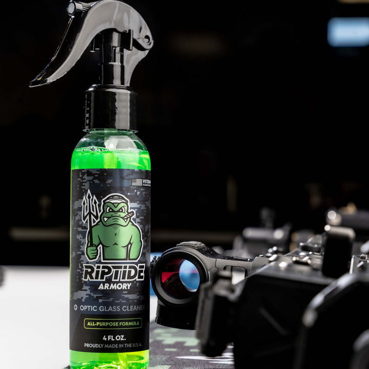 Bottle of Riptide Armory Optic Cleaner on a table equipment in the background